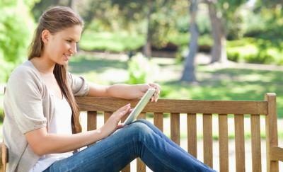 Femme lisant un livre électronique sur un banc de parc