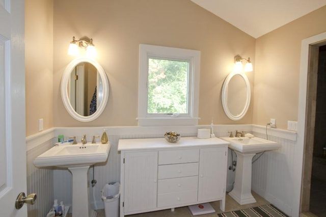 Une armoire blanche et la fenêtre entre deux piédestal en porcelaine puits dans une salle de bains.