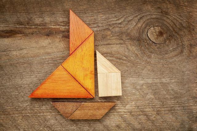 Un puzzle tangram sous la forme d'un voilier, la pose sur une table en bois.