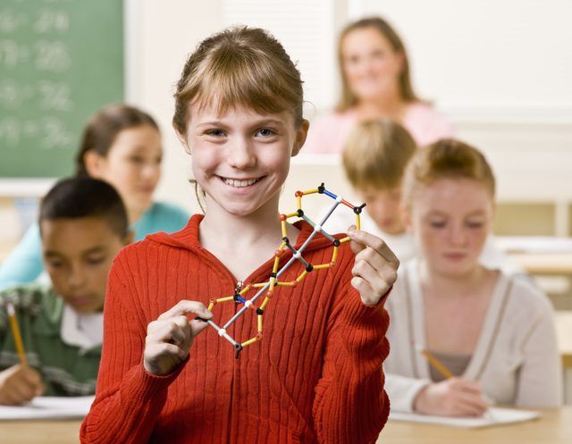 Un étudiant en souriant tenant un modèle en double hélice dans une salle de classe bondée.