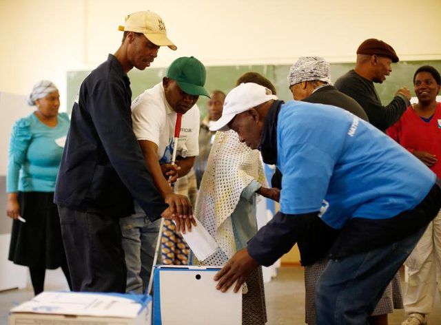 Un travailleur aide un aveugle mis son vote dans une boîte lors d'une élection en Afrique du Sud.
