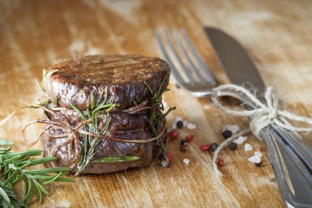 Une coupe de filet mignon grillé assaisonné avec du romarin et de poivre sur une planche de bois.