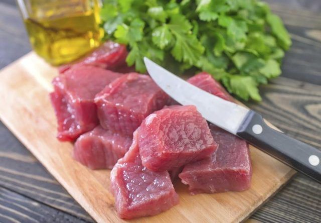 Cubes tranches de filet de bœuf crue sur une planche à découper avec le persil et l'huile d'olive.