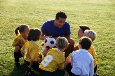 Un prof de gym explique le jeu de football pour les jeunes enfants sur un terrain.
