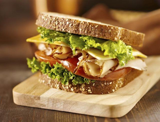 Un sandwich à la dinde avec de la laitue, fromage et tomate sur un pain de grains entiers.