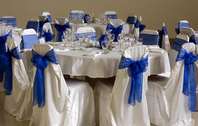Arcs de tulle bleu sont attachés autour tissu blanc drapé sur des chaises à une table de réception de mariage.
