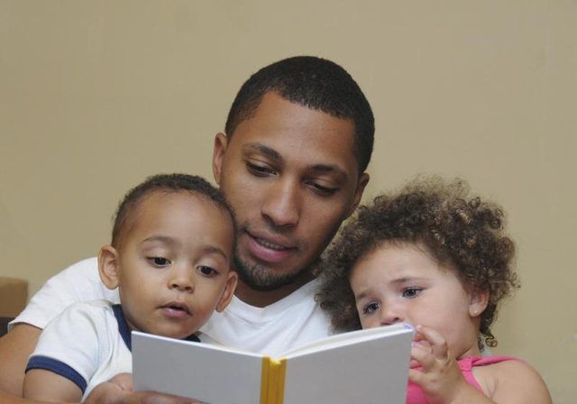 Un père lisant un livre à deux bambins.