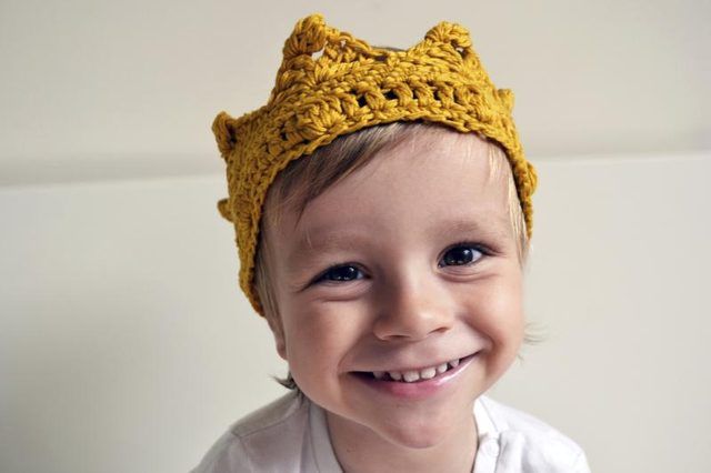 Un bambin souriant coiffé d'une couronne tricoté.