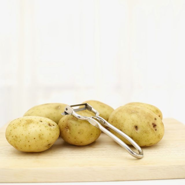 Petites pommes de terre et économe sur une planche à découper.