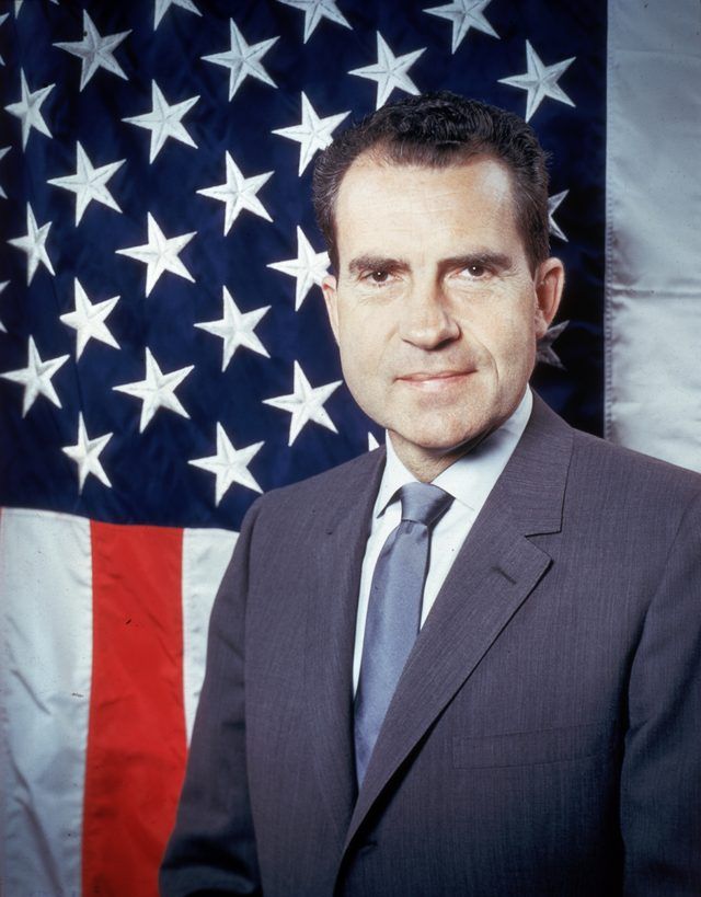 Portrait de Richard Nixon debout devant le drapeau américain.