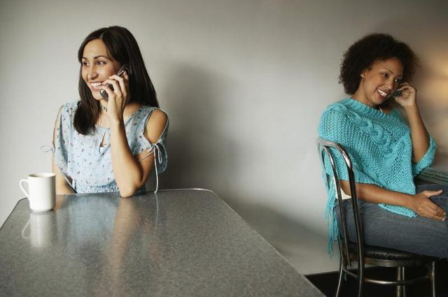 Deux femmes de parler sur les téléphones mobiles dans un café.