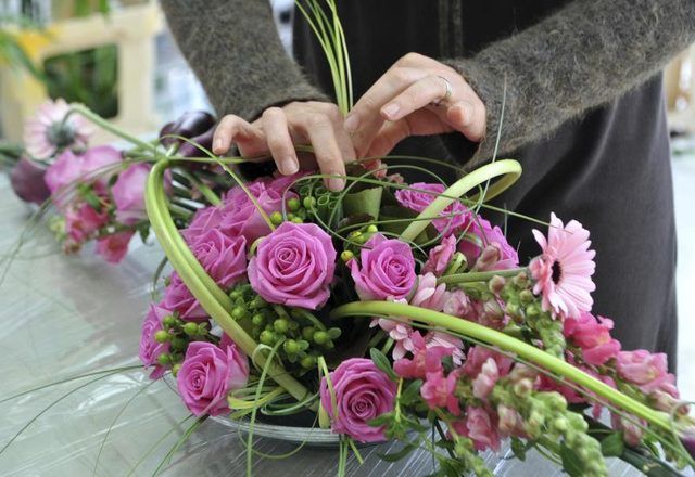 Un fleuriste organise un bouquet de roses roses.
