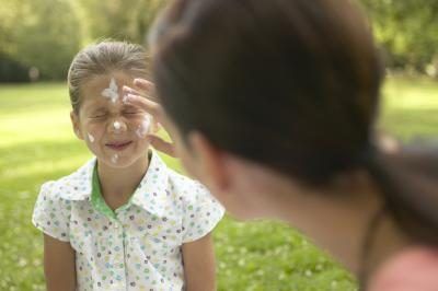 Une mère appliquer un écran solaire à sa fille's face outdoors.