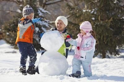 Une femme un bonhomme de neige à l'extérieur avec deux enfants.