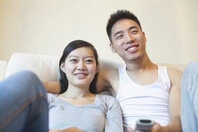Un couple sourit en regardant un film ensemble sur le canapé.