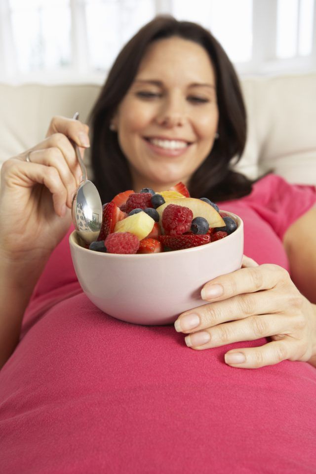 Une femme enceinte incline tout en mangeant un bol de fruits.