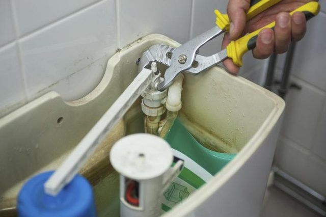 Un plombier répare une toilette avec une paire de pinces.