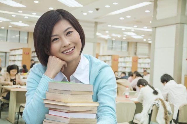 Femme étudiant avec une pile de livres dans la bibliothèque.